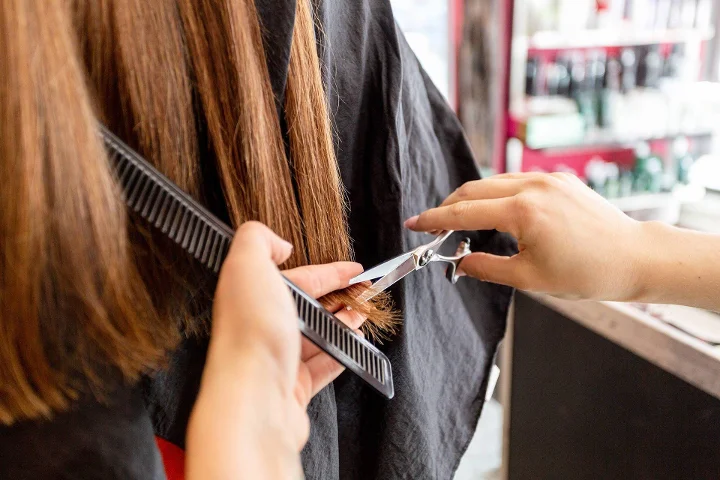 Mani che spuntano con forbici argentate capelli lunghi castani tenuti col pettine nero su una mantella scura in salone